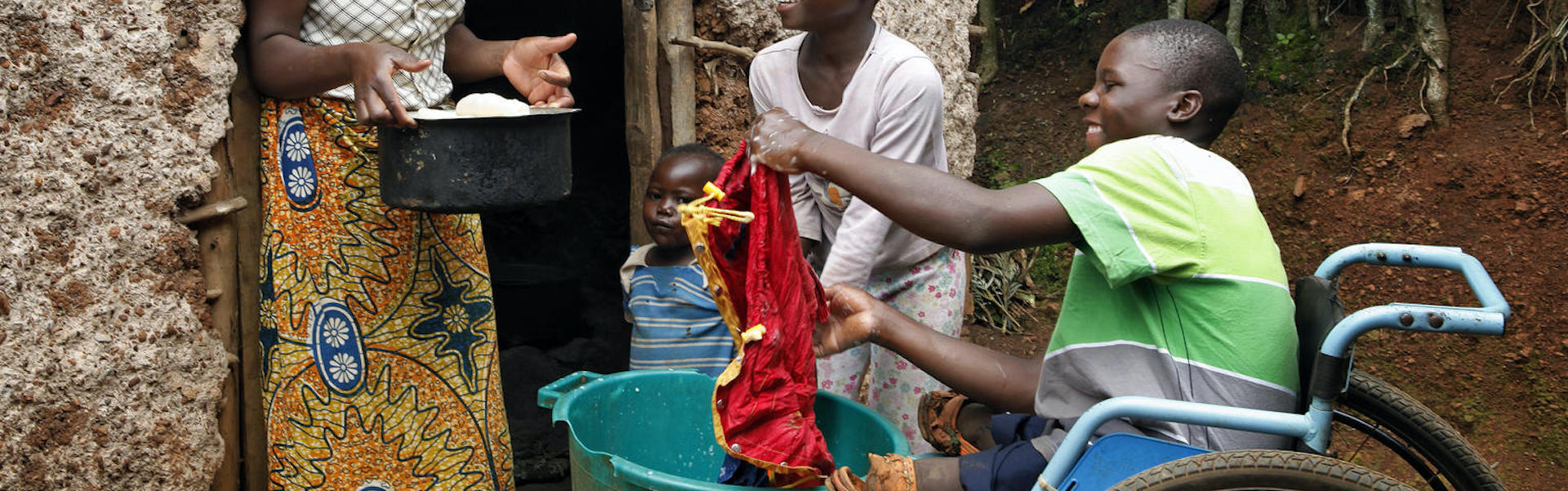A family outside their house of a mother and three younger people including one in a wheelchair.
