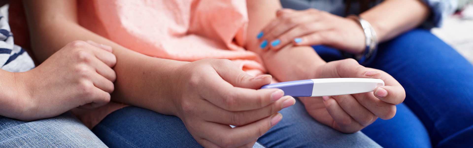 three young women seated looking at pregnancy kit held by one of them.